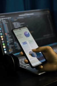 Developer coding React Native mobile application on laptop with smartphone displaying app interface