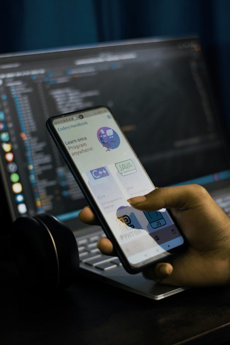 Developer coding React Native mobile application on laptop with smartphone displaying app interface
